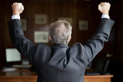 Businessman Celebrating Success With Arms Raised In Office