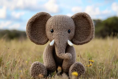 Knitted Elephant Toy Sitting In A Grassy Field