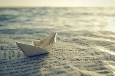 Paper Boat Sailing On A Sea Of Handwritten Text
