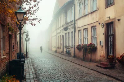Cyclist Riding Down A Foggy Cobblestone Street