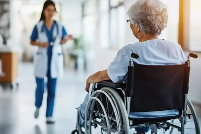 Elderly Patient Sitting In Wheelchair In Hospital Corridor