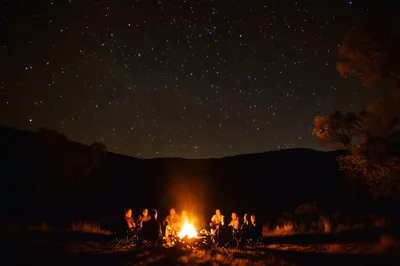 Group Of Friends Sitting Around A Campfire Under Starry Sky