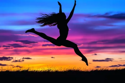 Silhouette Of A Woman Jumping Against A Sunset Sky