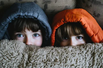 Two Children Peeking Out From Under A Blanket