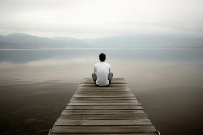 Man Sitting Alone On A Wooden Pier Overlooking A Lake