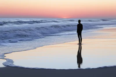 Surfer Standing Alone On Beach At Sunset