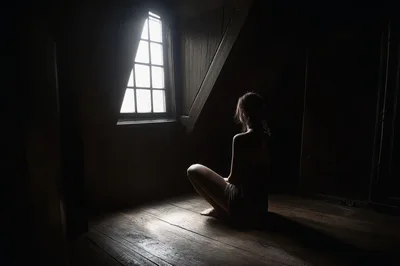 Young Woman Sitting Alone In A Dark Attic