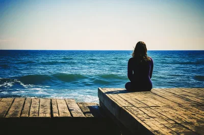 Woman Sitting Alone On A Wooden Pier By The Sea