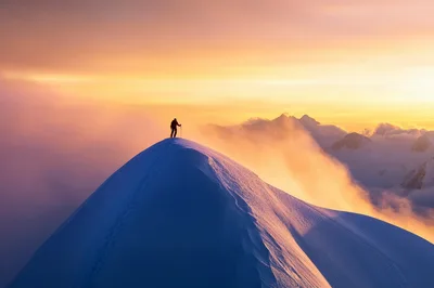 Mountaineer Standing On A Snowy Mountain Peak At Sunset