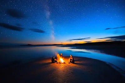 Friends Sitting Around A Campfire On A Beach At Night