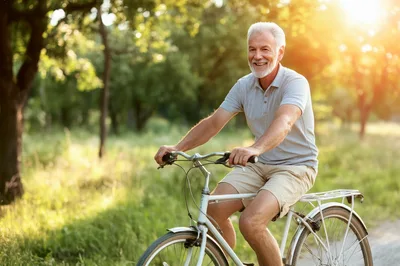 Senior Man Riding A Bicycle In A Sunny Park