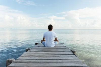 Man Meditating In Lotus Position On A Wooden Pier