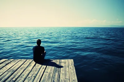 Man Sitting Alone On A Wooden Pier Overlooking The Ocean