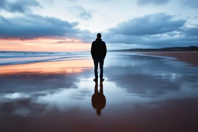 Man Standing Alone On A Reflective Beach At Sunset