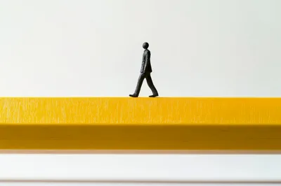 Miniature Business Figure Walking On A Yellow Pencil