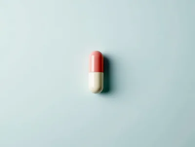 Single Pink and White Capsule Pill on Blue Background