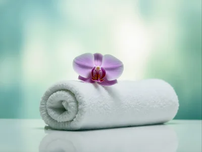 White Rolled Spa Towel With A Purple Orchid