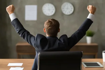 Businessman Celebrating Success With Arms Raised In Office