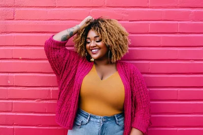 Smiling Woman With Curly Hair Posing Against Pink Wall