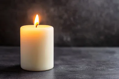 Lit White Pillar Candle on Dark Textured Surface