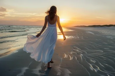 Woman In White Dress Walking On Beach At Sunset