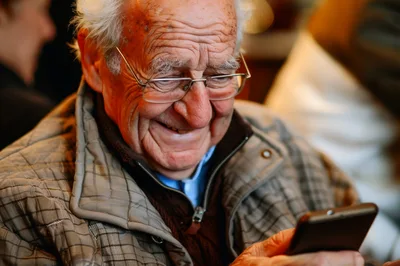 Elderly Man Smiling While Using A Smartphone
