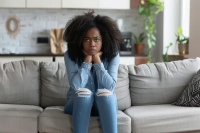 Pensive Young Woman Sitting On A Sofa