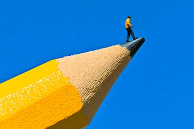 Miniature Person Walking On A Giant Pencil Tip