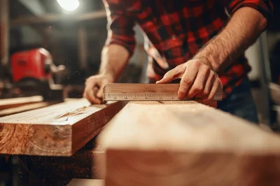 Carpenter Measuring Wooden Plank In Workshop