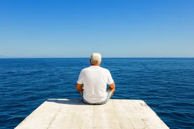 Senior Man Sitting On A Pier Overlooking The Ocean
