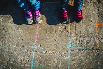 Children Standing On A Chalk Drawn Hopscotch Grid