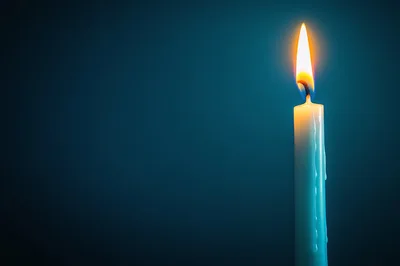 Single Lit Candle Against Dark Blue Background