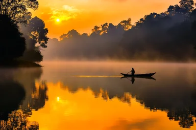 Lone Fisherman Rowing Boat on Misty River at Sunrise