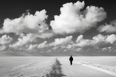 Lone Person Walking Along Snowy Path Under Dramatic Clouds