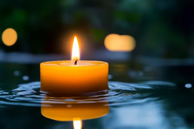 Floating Yellow Candle On Dark Water Surface