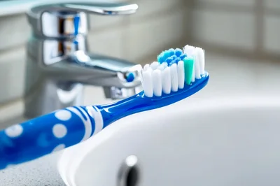 Blue Toothbrush Resting Near Bathroom Sink Faucet