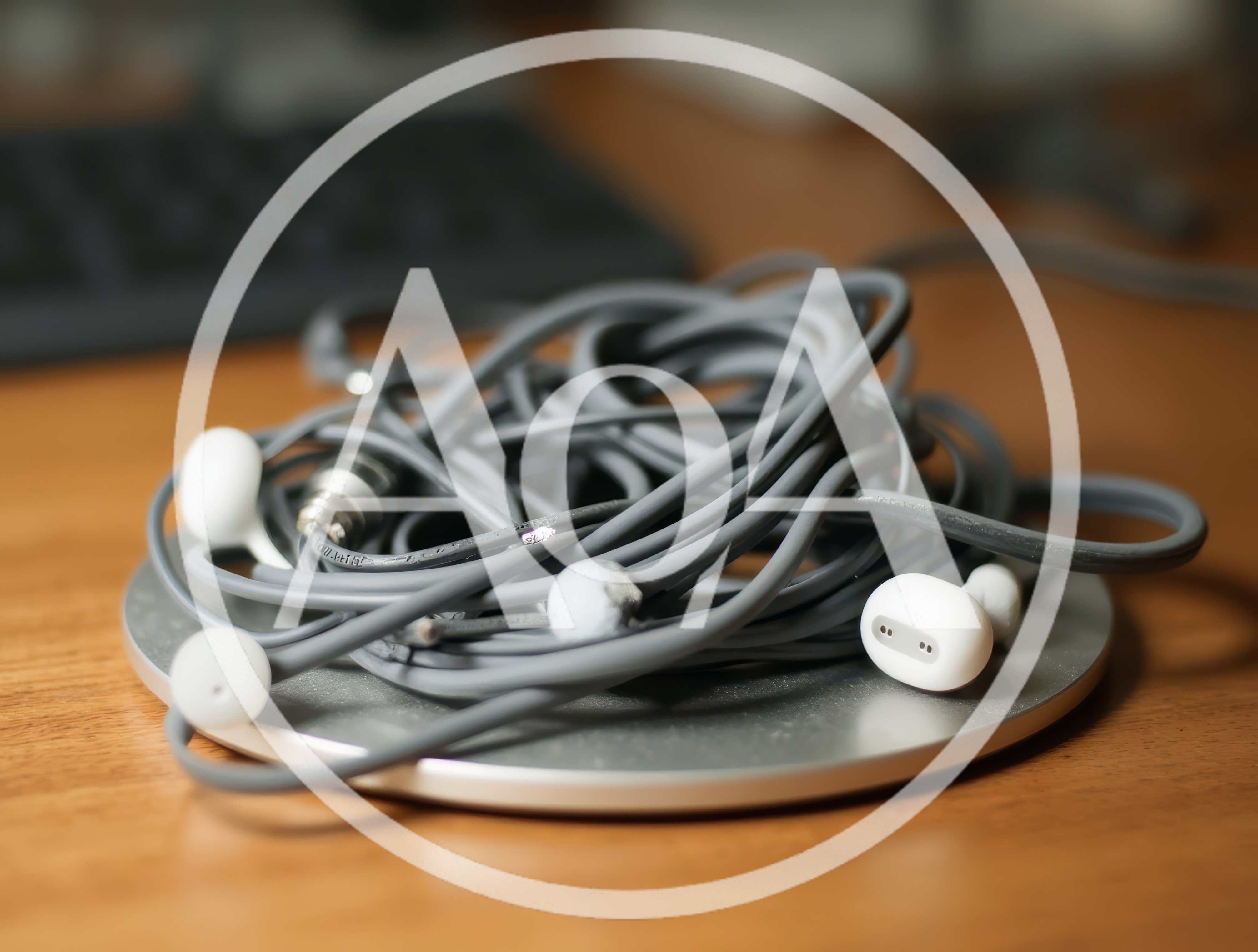 Tangled Gray Wired Earbuds On A Metal Desk Stand