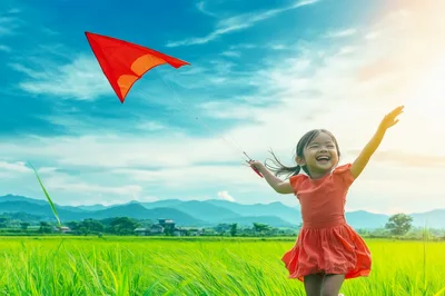 Happy Young Girl Flying Red Kite in Green Field