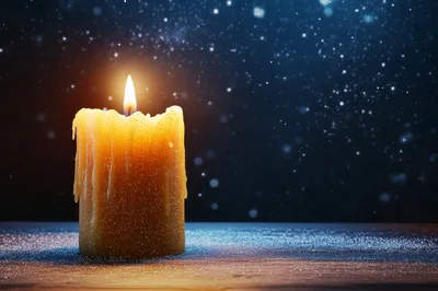 Lit Candle On A Snowy Surface At Night