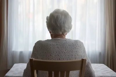 Elderly Woman Sitting Alone Facing A Bright Window
