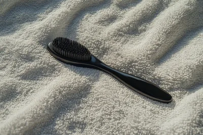 Black Hair Brush Resting On A White Towel
