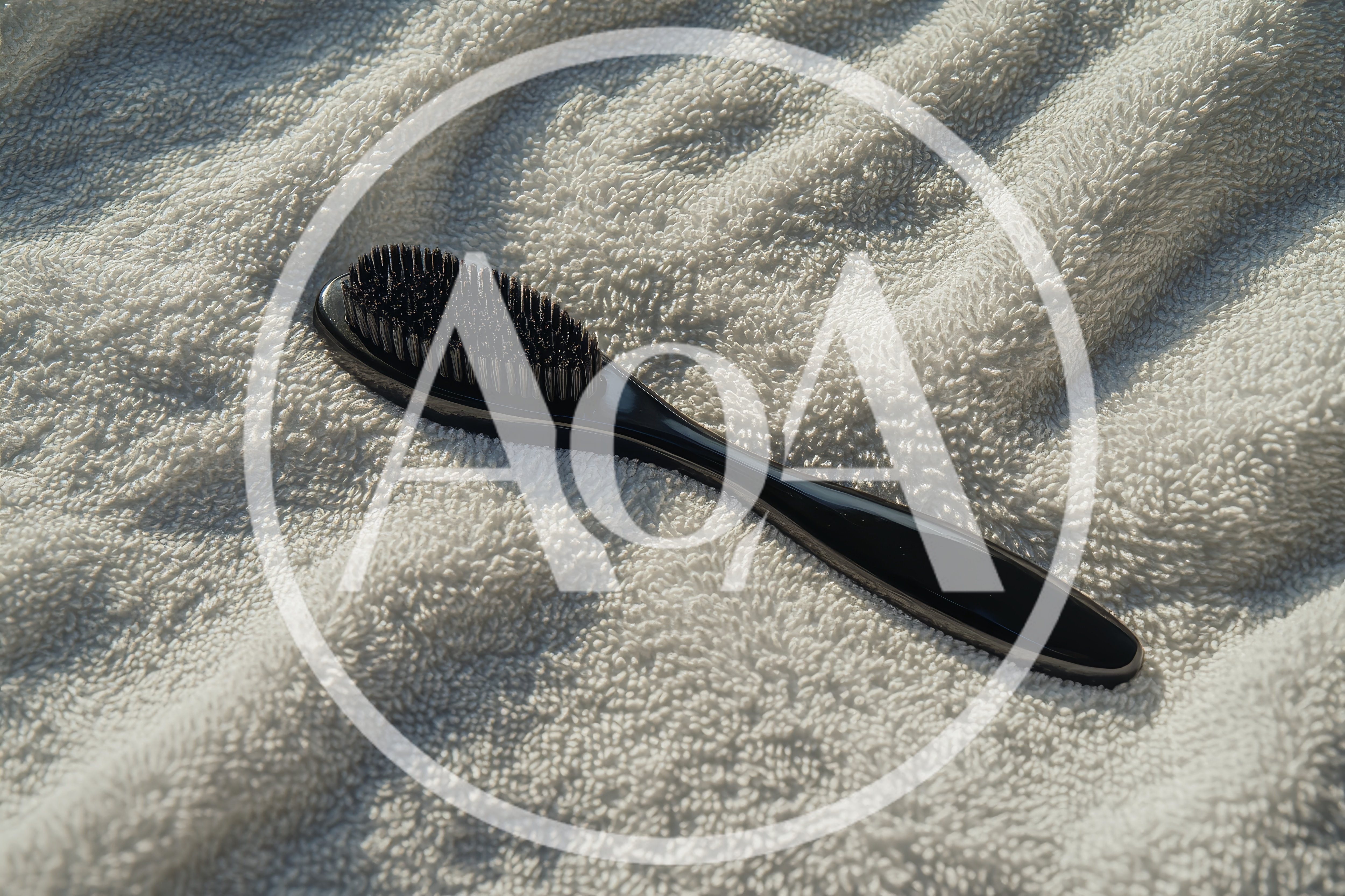 Black Hair Brush Resting On A White Towel
