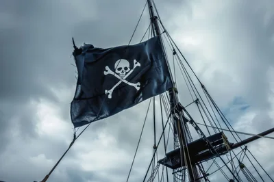 Tattered Jolly Roger Pirate Flag Flying On Ship Mast