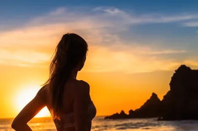 Woman Silhouetted Against A Golden Sunset At The Beach