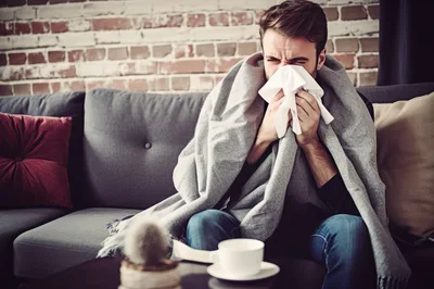 Sick Man Blowing Nose While Wrapped In Blanket