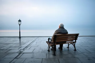 Elderly Man Sitting Alone On A Bench By The Sea