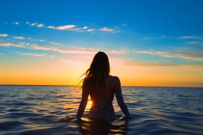 Woman Standing In Ocean At Sunset