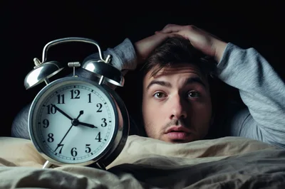 Stressed Man Awake In Bed With Alarm Clock