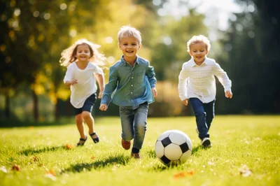 Three Happy Children Playing Soccer In A Sunny Park