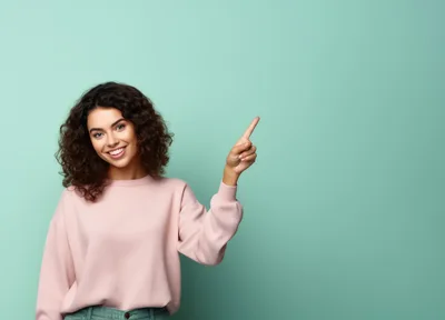 Smiling Young Woman Pointing Upwards Against Teal Background